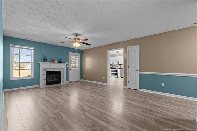 unfurnished living room featuring a fireplace, a textured ceiling, light hardwood / wood-style flooring, and ceiling fan