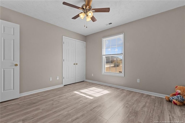 unfurnished bedroom with ceiling fan, light hardwood / wood-style flooring, a closet, and a textured ceiling