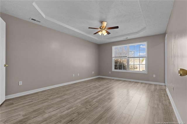 spare room with ceiling fan, a tray ceiling, a textured ceiling, and light wood-type flooring