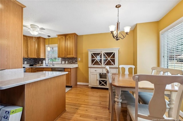 kitchen featuring ceiling fan with notable chandelier, decorative light fixtures, tasteful backsplash, sink, and light wood-type flooring