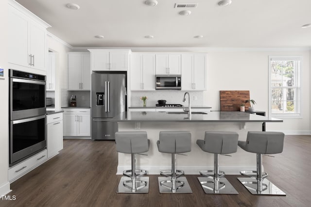 kitchen featuring stainless steel appliances, a sink, visible vents, ornamental molding, and a kitchen bar