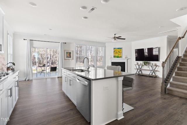 kitchen with a center island with sink, crown molding, stainless steel dishwasher, a fireplace, and a sink