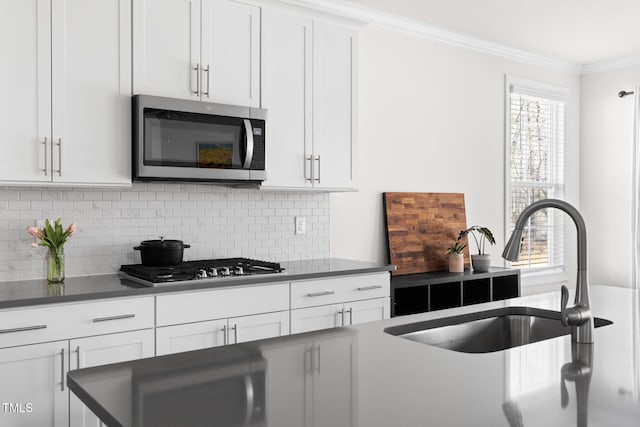 kitchen featuring a sink, white cabinetry, appliances with stainless steel finishes, decorative backsplash, and crown molding