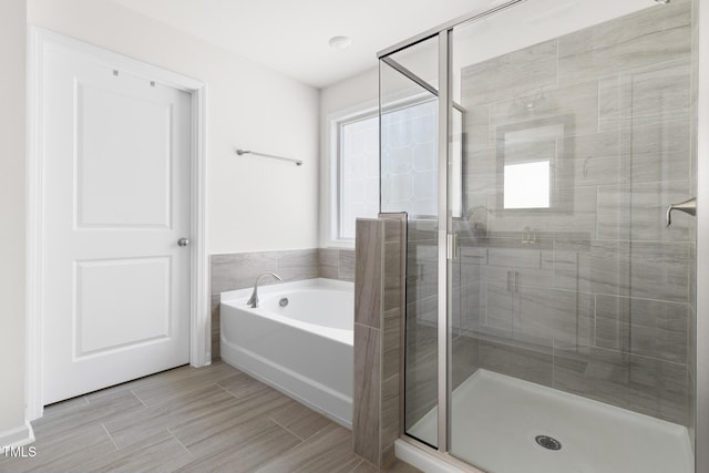 bathroom with a stall shower, a bath, and wood finish floors