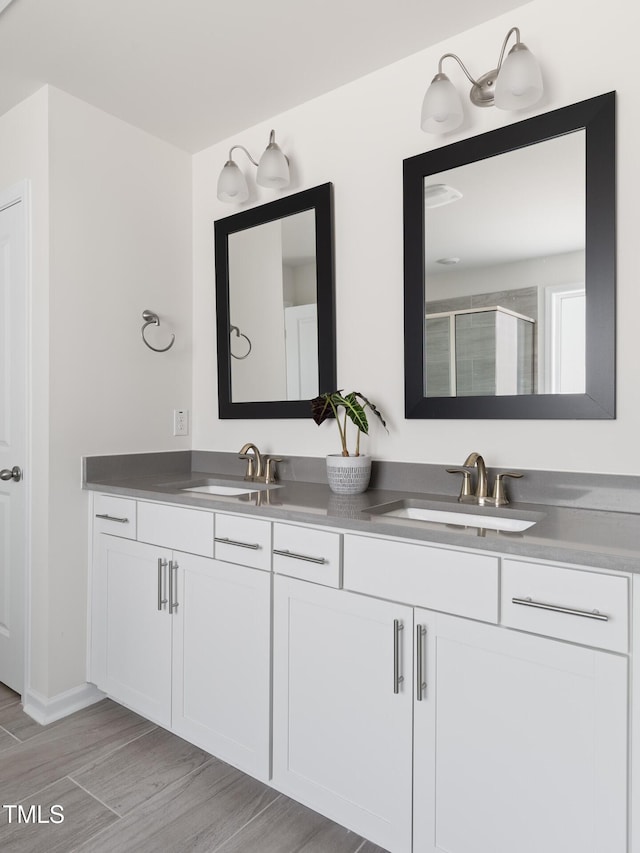 bathroom with a stall shower, wood finished floors, a sink, and double vanity