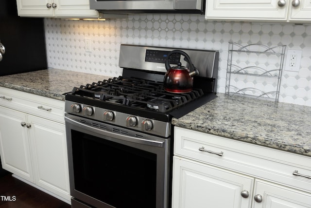 kitchen with light stone countertops, backsplash, white cabinets, and stainless steel gas range