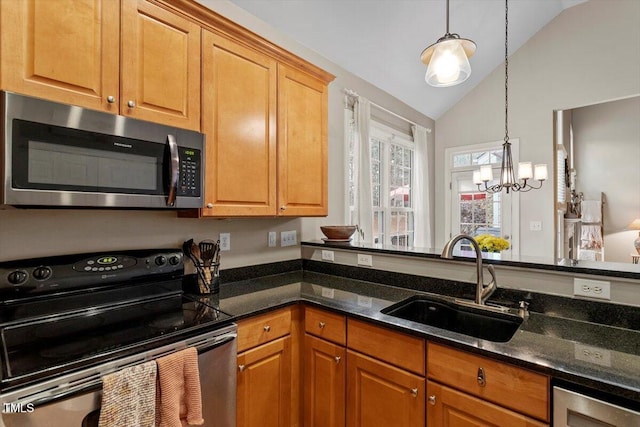 kitchen with dark stone counters, stainless steel appliances, a sink, and pendant lighting