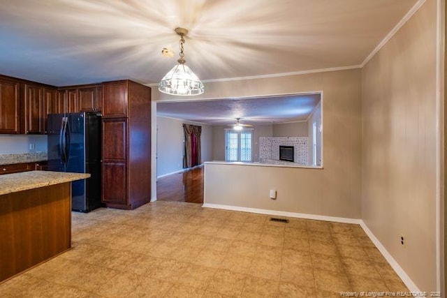 kitchen with ceiling fan, black refrigerator, hanging light fixtures, light stone counters, and ornamental molding