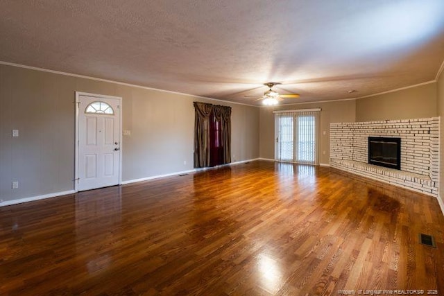 unfurnished living room featuring hardwood / wood-style floors, ceiling fan, crown molding, a brick fireplace, and a textured ceiling