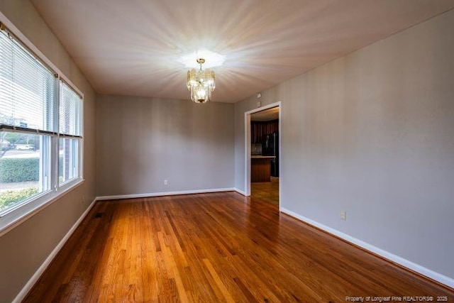 empty room with hardwood / wood-style floors and a chandelier