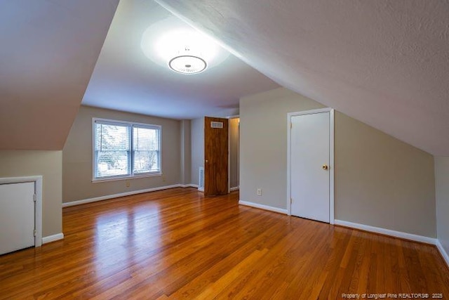 bonus room with wood-type flooring, a textured ceiling, and vaulted ceiling