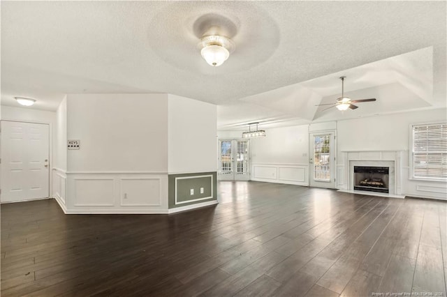 unfurnished living room with dark wood-type flooring, ceiling fan, a tray ceiling, and a textured ceiling