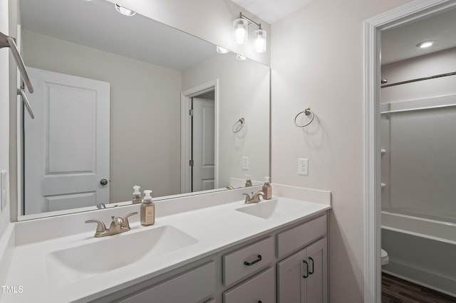 full bath with double vanity, wood finished floors, a sink, and toilet