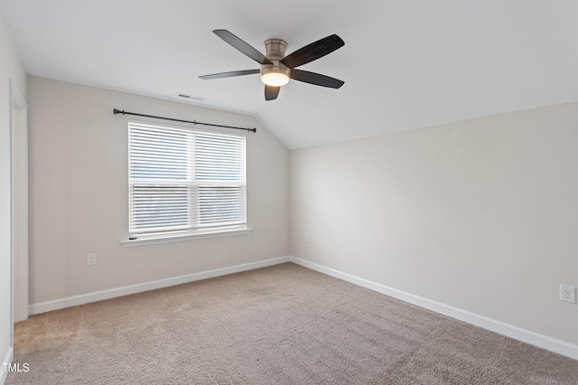 carpeted spare room featuring baseboards, visible vents, vaulted ceiling, and a ceiling fan