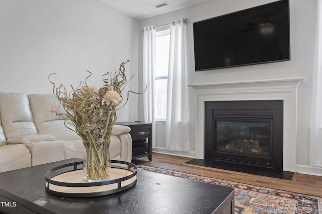 living room with a fireplace with flush hearth, wood finished floors, and visible vents