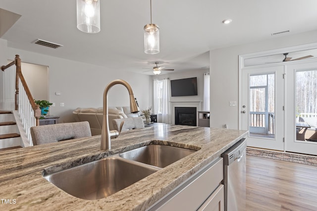 kitchen featuring dishwasher, a sink, visible vents, and light stone countertops