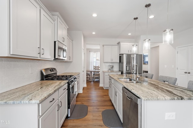 kitchen featuring stainless steel appliances, a sink, light wood-style floors, hanging light fixtures, and an island with sink