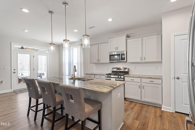 kitchen with backsplash, appliances with stainless steel finishes, a sink, an island with sink, and a kitchen breakfast bar