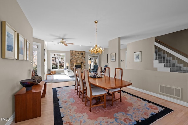 dining room featuring light wood-style flooring, ceiling fan with notable chandelier, a fireplace, visible vents, and baseboards