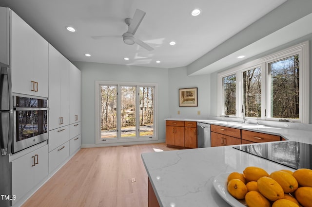 kitchen featuring light stone counters, stainless steel appliances, a sink, white cabinetry, and brown cabinetry