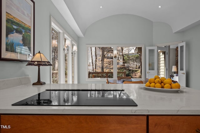 kitchen featuring lofted ceiling, light stone counters, and black electric cooktop