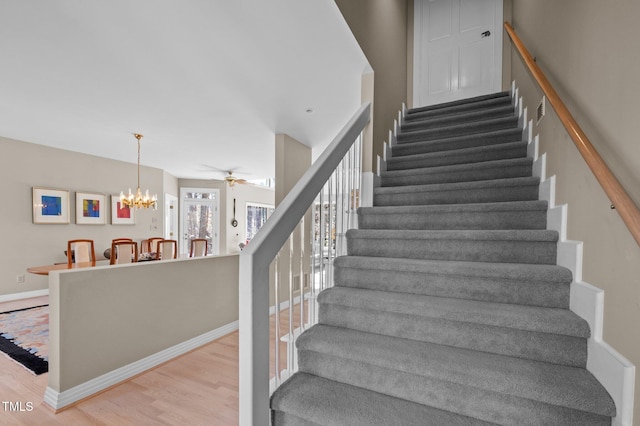 stairs featuring ceiling fan with notable chandelier, wood finished floors, and baseboards