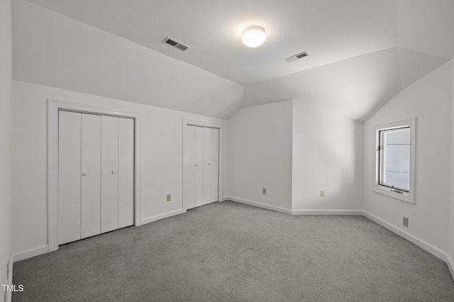 unfurnished bedroom with light colored carpet, visible vents, vaulted ceiling, and two closets