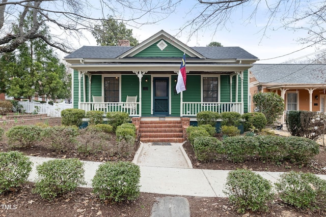 bungalow-style home featuring fence, covered porch, and a shingled roof