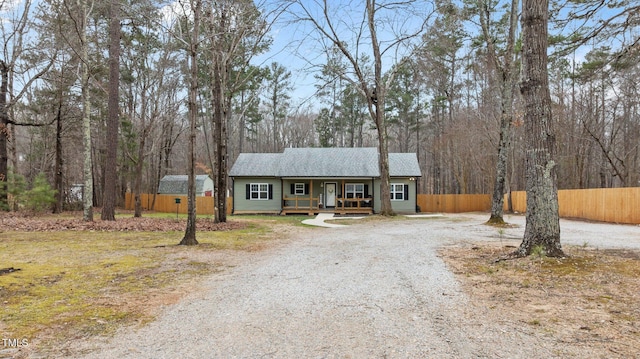 view of front of house featuring a porch, gravel driveway, fence, and a shingled roof