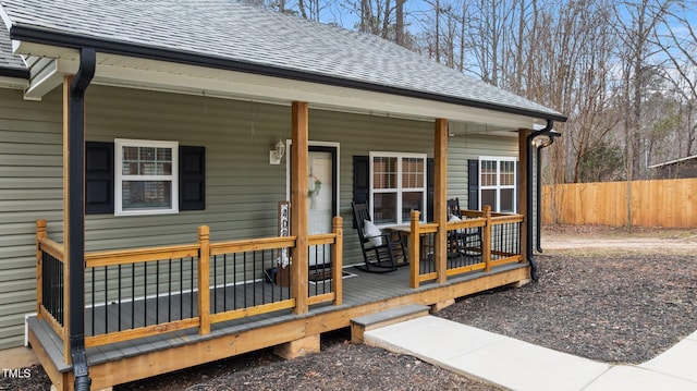 exterior space with covered porch, roof with shingles, and fence