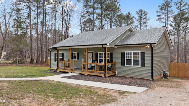 bungalow featuring covered porch, fence, a front lawn, and roof with shingles