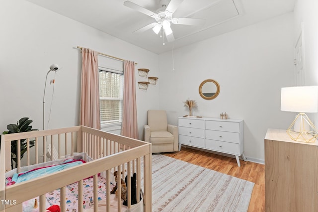 bedroom featuring light wood-style floors, ceiling fan, and a crib