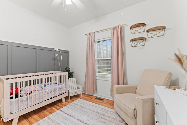 bedroom with a nursery area, ceiling fan, a decorative wall, and light wood-style floors