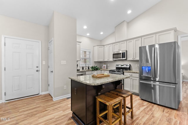 kitchen featuring appliances with stainless steel finishes, a kitchen island, light stone countertops, light wood-type flooring, and a kitchen bar