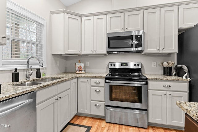 kitchen with light wood finished floors, stainless steel appliances, white cabinetry, a sink, and light stone countertops