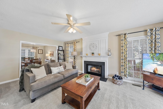 living area featuring light carpet, a large fireplace, a textured ceiling, and a ceiling fan