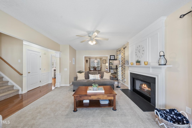 living room with a fireplace with flush hearth, ceiling fan, stairs, a textured ceiling, and carpet flooring