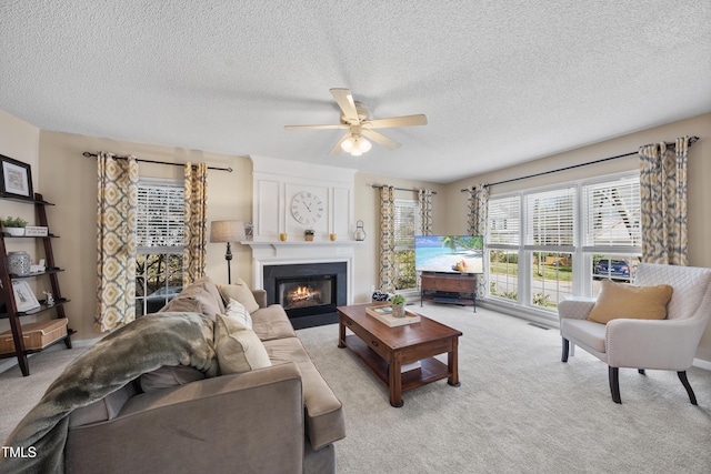 living room featuring a ceiling fan, a large fireplace, light colored carpet, and a textured ceiling