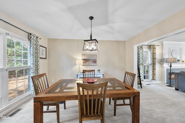 dining space with carpet, a lit fireplace, visible vents, and a textured ceiling