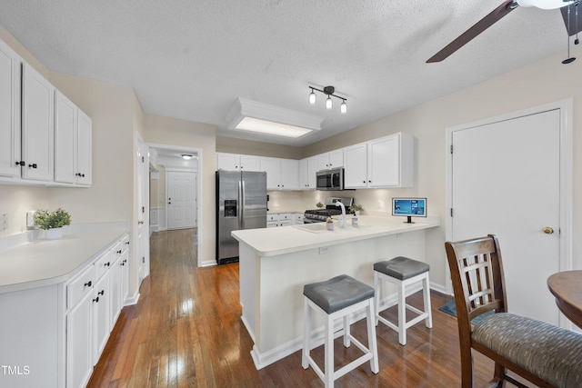 kitchen with dark wood finished floors, stainless steel appliances, light countertops, a peninsula, and a kitchen breakfast bar