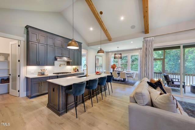 kitchen featuring decorative light fixtures, stainless steel gas stovetop, sink, a kitchen island with sink, and light hardwood / wood-style floors