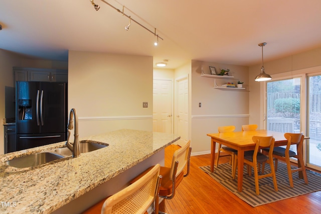 kitchen featuring a sink, refrigerator with ice dispenser, light stone counters, and hanging light fixtures