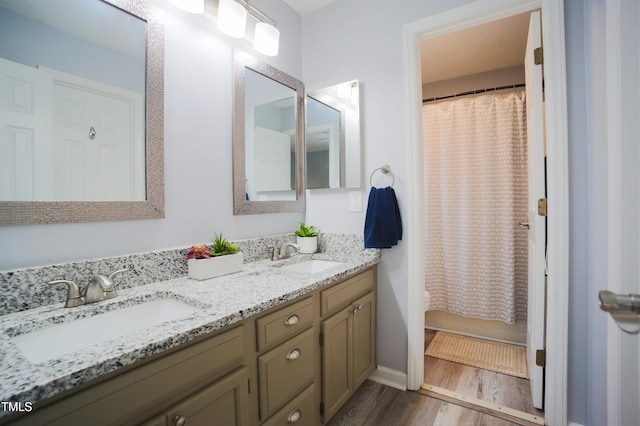 bathroom featuring double vanity, a sink, a shower with shower curtain, and wood finished floors