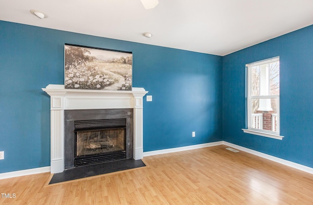 unfurnished living room with a fireplace with flush hearth, visible vents, baseboards, and wood finished floors