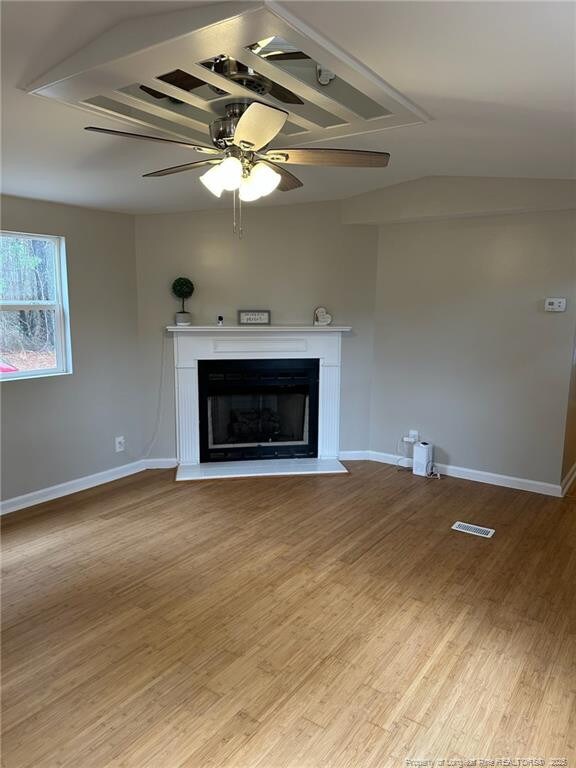 unfurnished living room with a fireplace, wood finished floors, visible vents, and baseboards