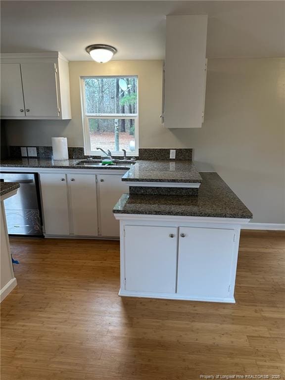 kitchen with light wood finished floors, white cabinets, a peninsula, stainless steel dishwasher, and a sink