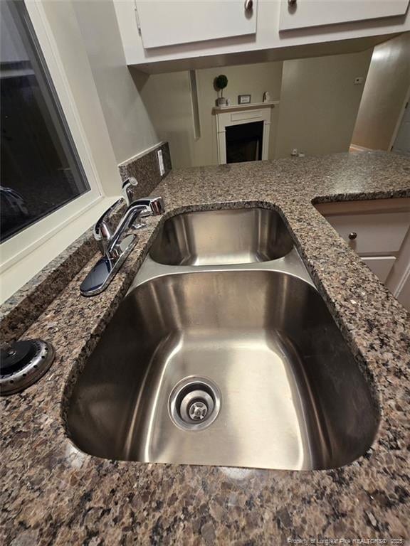 interior details with a fireplace, white cabinets, a sink, and dark stone countertops