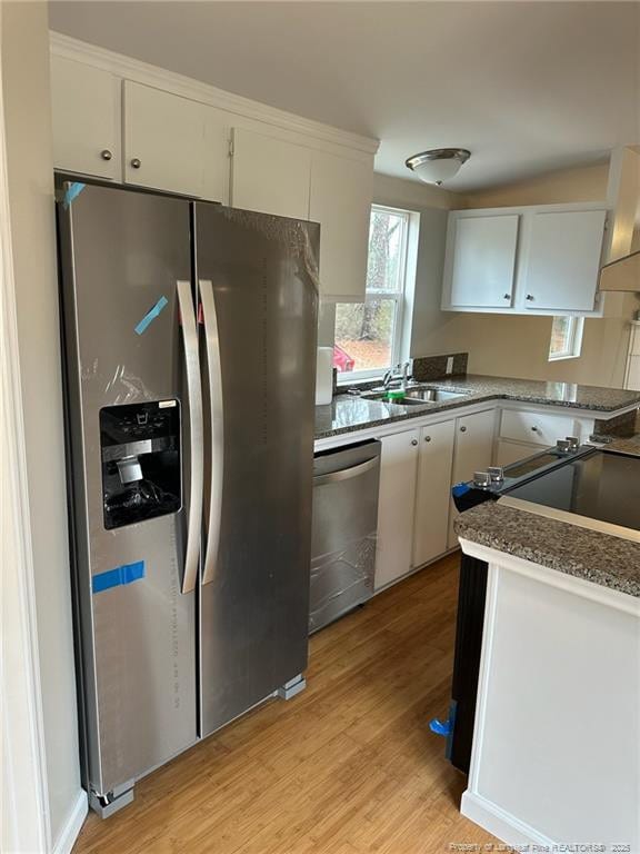 kitchen with stainless steel appliances, white cabinets, a sink, and light wood-style flooring