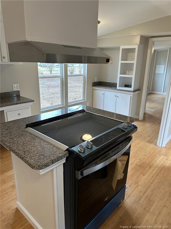 kitchen with light wood-style flooring, white cabinets, black range with electric stovetop, and wall chimney range hood