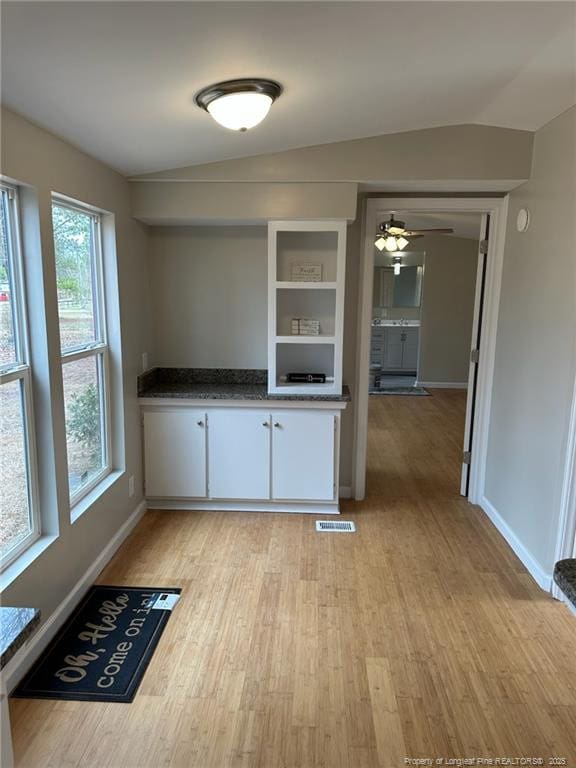 kitchen with lofted ceiling, light wood finished floors, baseboards, and white cabinetry